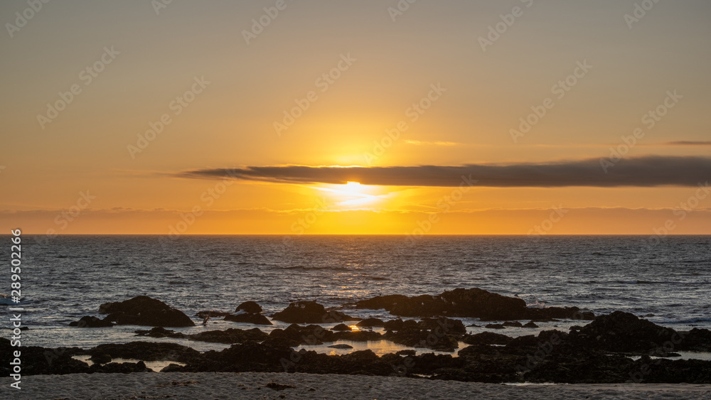 Beautiful sunset over ocean with bright orange sky and shining sun behind cloud on horizon