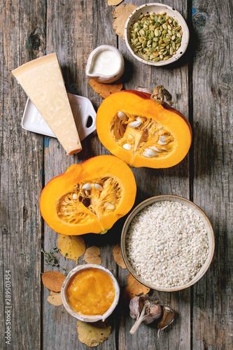 Ingredients for cooking pumpkin risotto. Raw uncooked risotto rice in ceramic bowl, sliced pumpkin, cream, seeds, parmesan cheese, garlic and autumn leaves over dark wooden background. Flat lay, space