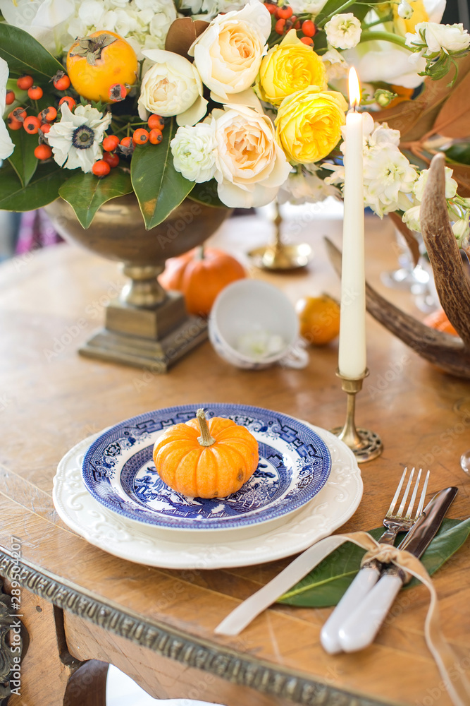 Luxurious elegant wedding decor in autumn style. Wooden vintage table setting with ceramic plates and silver cutlery. Fresh flowers in a vase, orange pumpkins, deer horns and candles. Romantic dinner. Luxurious elegant wedding decor in autumn style. Wooden vintage table setting with ceramic plates and silver cutlery. Fresh flowers in a vase, orange pumpkins, deer horns and candles. Romantic dinner.