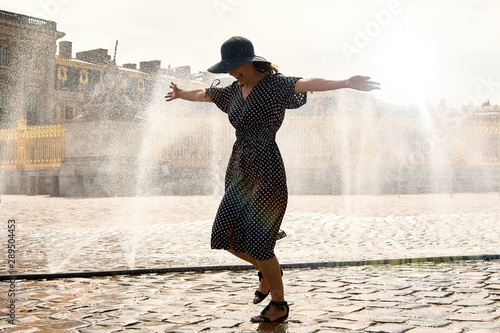 Принти на полотні Happy girl in dress and hat in a spray of water on a sunny summer day, Versaille