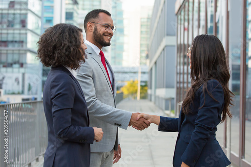 Side view of positive business people handshake. Business man and women standing in city street, shaking hands, smiling and talking. Welcoming concept