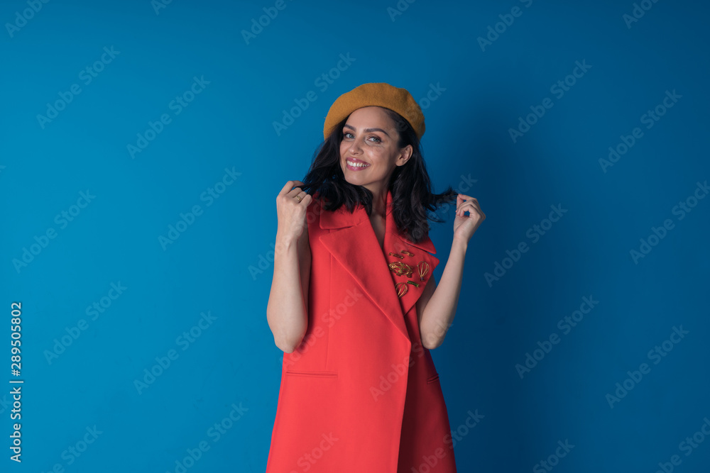 Naklejka premium Portrait of a happy girl in a stylish beret and red vest, like a Frenchwoman on a blue background