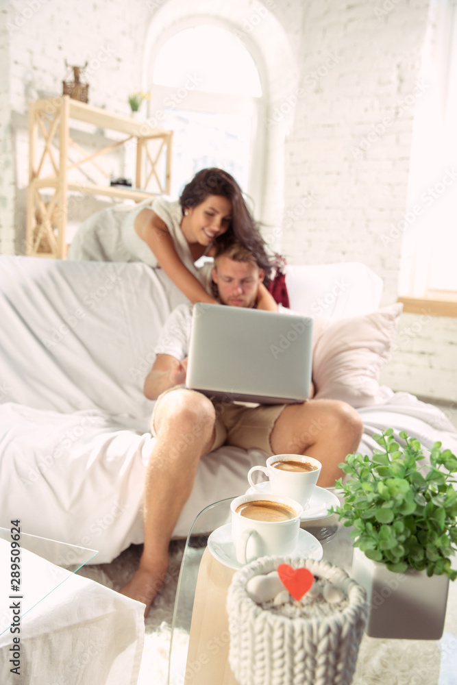 Couple of lovers at home relaxing together. Caucasian man and woman having weekend, looks tender and happy. Concept of relations, family, autumn and winter comfort. Watching cinema and laughting. Couple of lovers at home relaxing together. Caucasian man and woman having weekend, looks tender and happy. Concept of relations, family, autumn and winter comfort. Watching cinema and laughting.