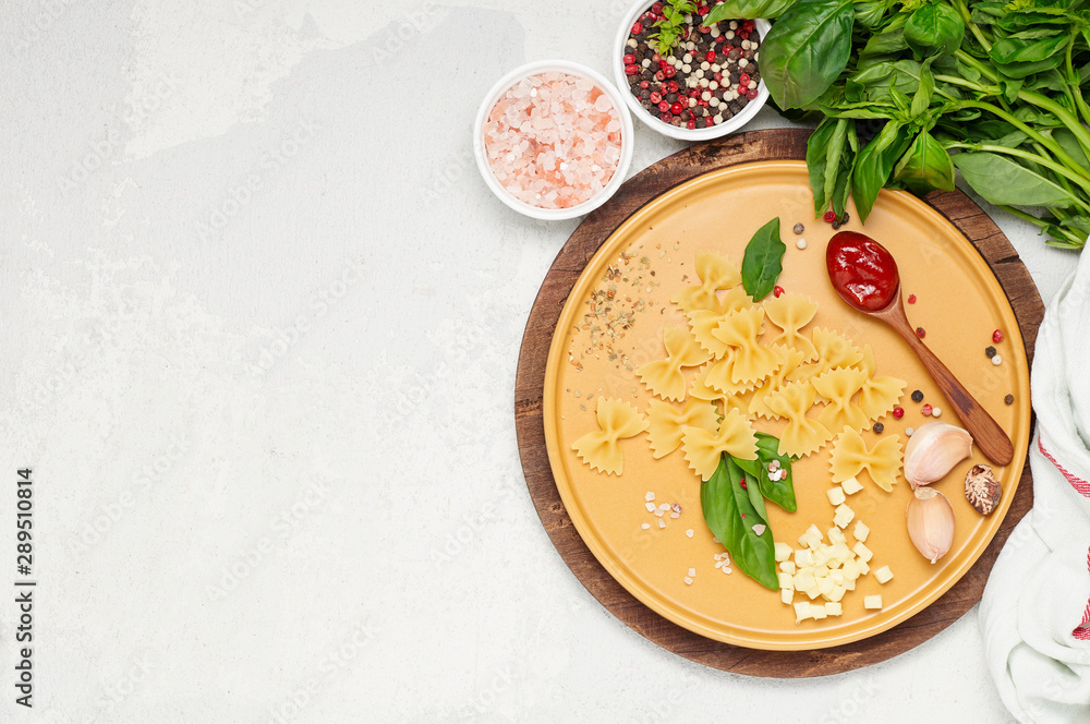 Ingredient for simple italian dinner on yellow plate. Farfalle, fresh basil, tomato souce, garlic and mozzarella cheese