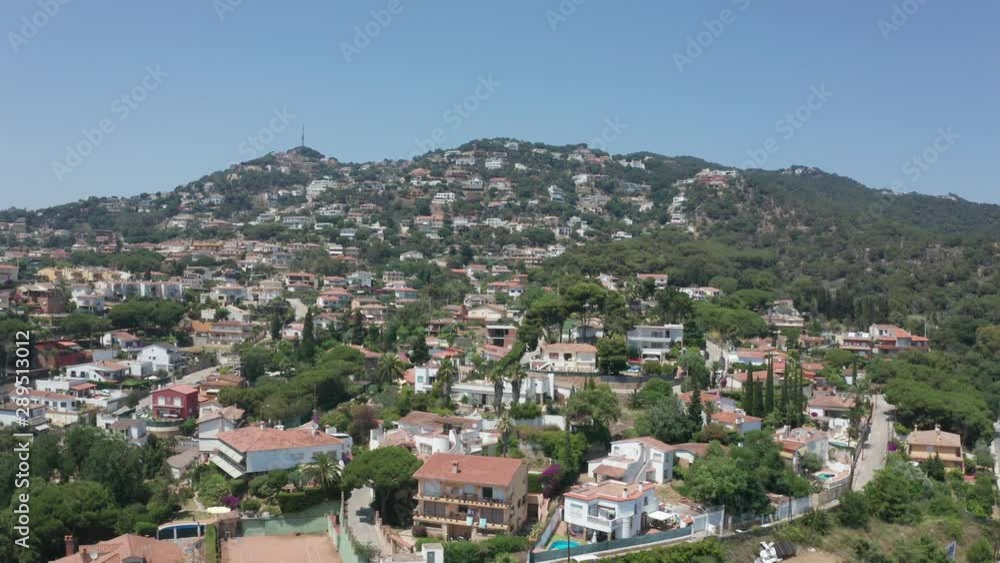 Aerial view of spanish coastal town on background of green mountain hills. Drone shot of scenic cityscape, cozy mansions among green trees in small mediterranean town Lloret de Mar, Catalonia, Spain Aerial view of spanish coastal town on background of green mountain hills. Drone shot of scenic cityscape, cozy mansions among green trees in small mediterranean town Lloret de Mar, Catalonia, Spain
