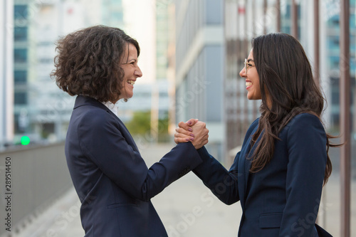 Happy businesswomen celebrating team success. Business ladies giving friendly handshake. Corporate success concept