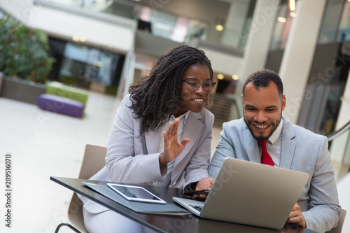 Cheerful coworkers using laptop. Smiling young African American business people sitting at table and using digital devices. Technology concept