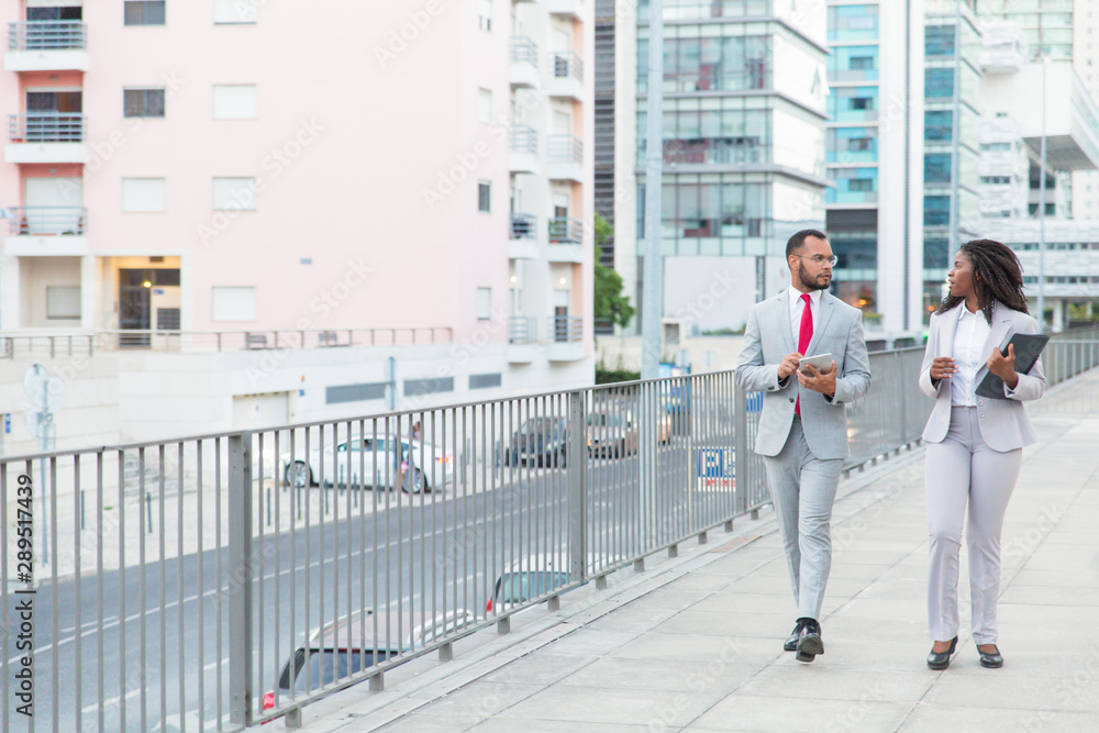 Serious African American coworkers on street. Professional young businessman and businesswoman walking and talking outside office building. Cooperation concept Serious African American coworkers on street. Professional young businessman and businesswoman walking and talking outside office building. Cooperation concept