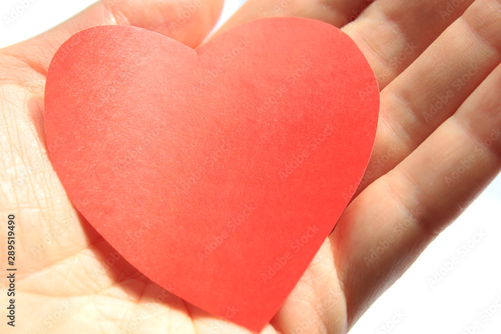 Obraz premium A bright red heart made of paper lies on the palm of your hand.