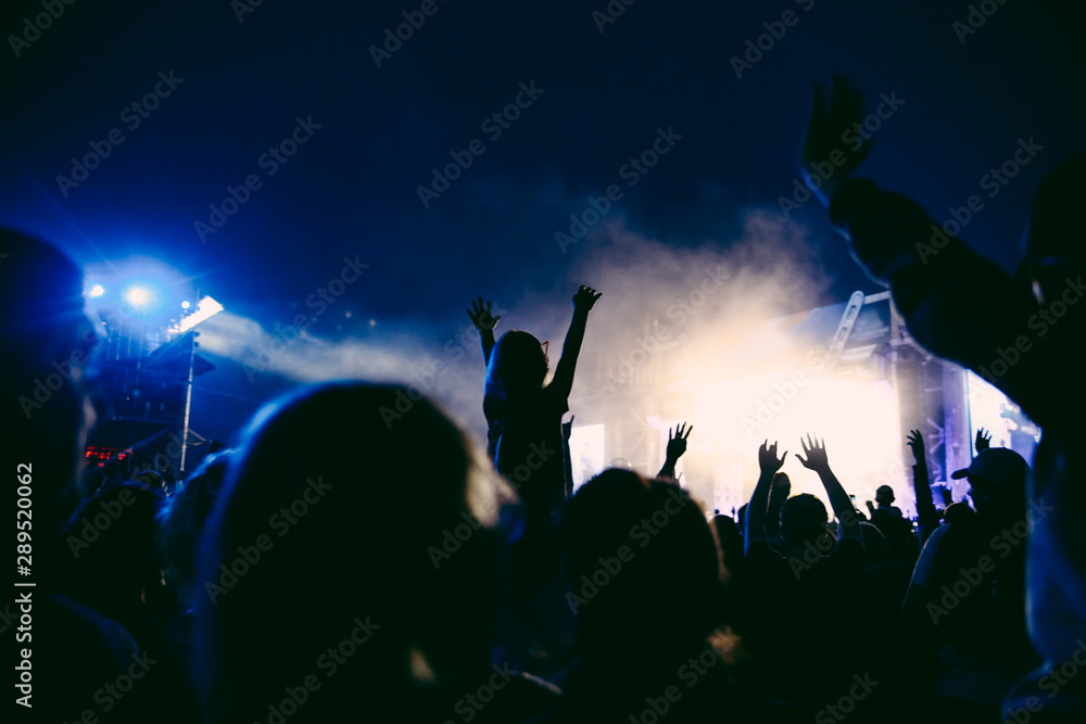 Silhouettes of raised hands on the concert in the night. Little girl with the hands up is sitting on the neck. The crowd of people at the open air music festival. Music background.