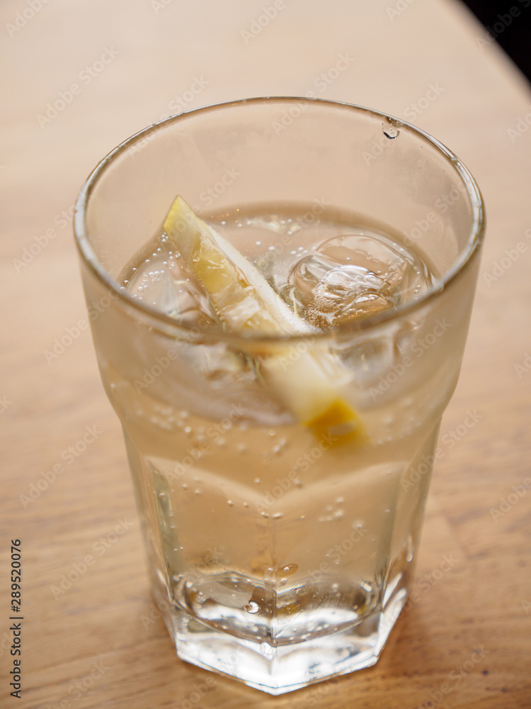 Closeup macro detail of an ice-cold glass of soda with a lemon wedge on a wooden table at a seaside cafe. Vertical orientation, shallow focus. St. Ives, England. Travel and drinks. Closeup macro detail of an ice-cold glass of soda with a lemon wedge on a wooden table at a seaside cafe. Vertical orientation, shallow focus. St. Ives, England. Travel and drinks.
