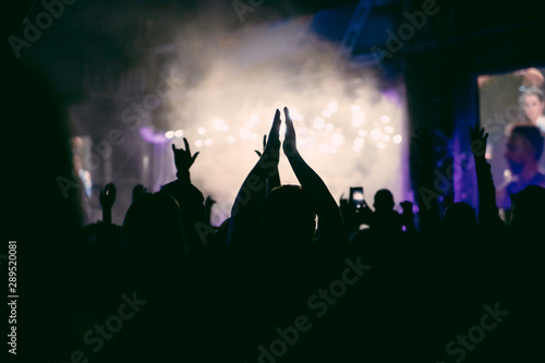 Silhouettes of raised and applauding hands on the concert in the night. The crowd of people at the open air music festival. Music background.