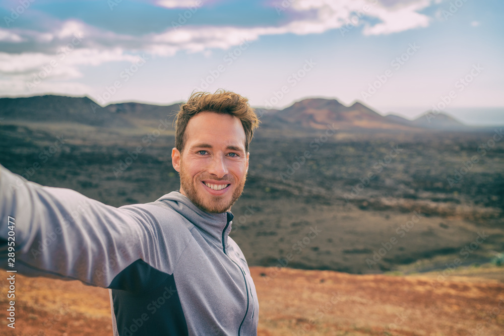 Selfie tourist man hiking in volcano mountain landscape black volcanic rocks. Happy smiling youn adventure hiker in summer travel destination.