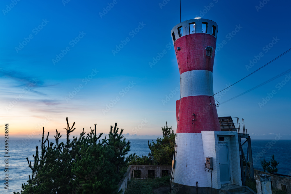 朝の小島の岬の先の赤い灯台