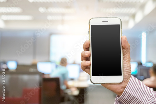 Close up hand holding white smartphone on blank screen at office blur background clipping path inside