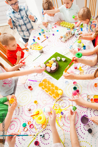Many kids sitting at the table and create Ester decorations