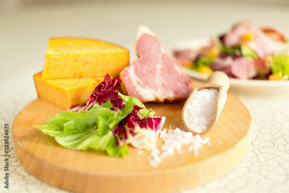 A plate of salad of green leaves, ham and cheese. Plate of salad with green leaves, ham and cheese. Fresh lettuce, cheese, ham and sea salt on a cutting board. Intercontinental breakfast at the hotel.