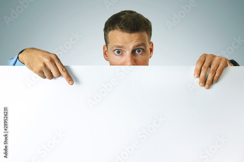 surprised man pointing on white blank poster with copy space