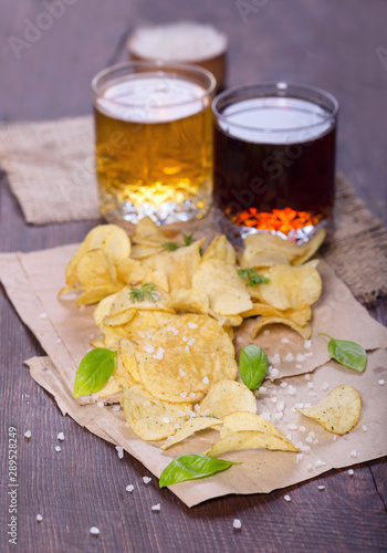Potato chips with salt and greens on a table in a pub on a background of beer. Chips with greens as a snack to beer. October Beer Fest.