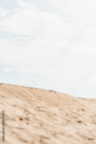 selective focus of wavy and golden sand against sky with clouds in desert