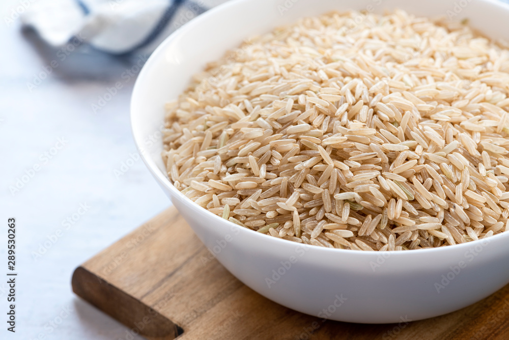Dry uncooked brown rice in a white bowl closeup. Thai cuisine, vegetarian food. Dry uncooked brown rice in a white bowl closeup. Thai cuisine, vegetarian food.