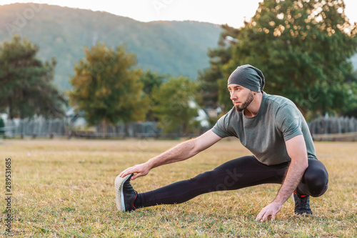Sports and yoga. A man with a beard, in sportswear performs stretching on the grass before training. Copy space