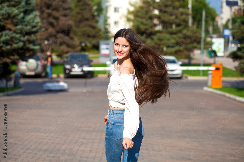 Young beautiful brunette woman in jeans and white blouse walking in summer street