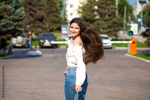 Young beautiful brunette woman in jeans and white blouse walking in summer street
