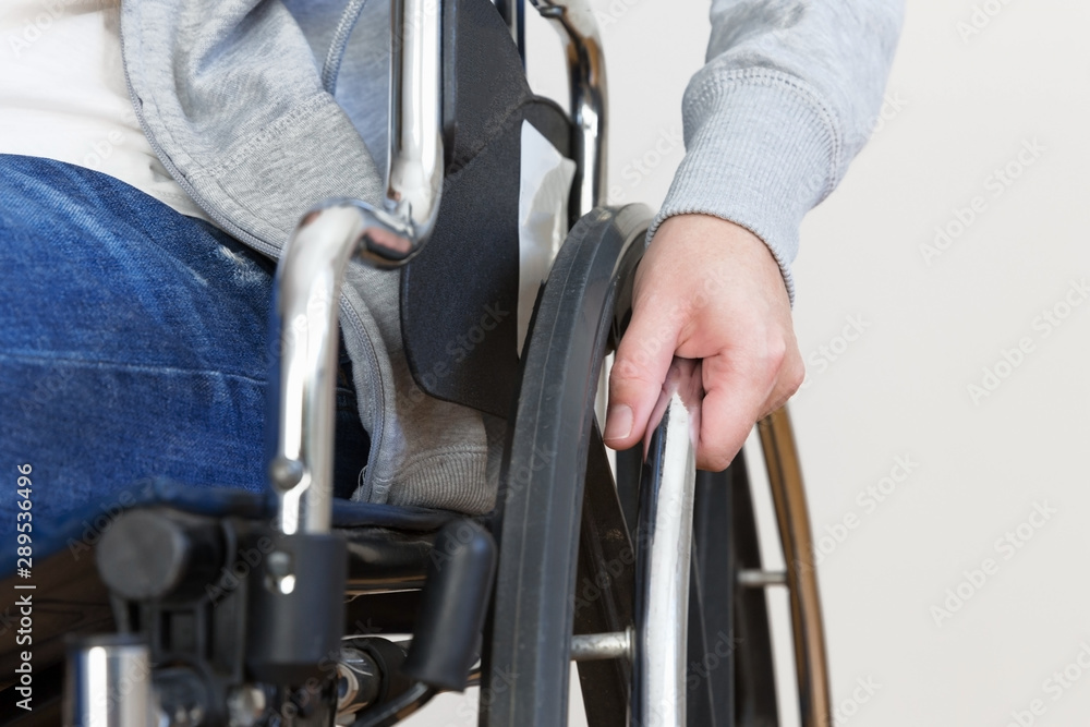 Detail of disabled woman holding a hand on wheel of a wheelchair.