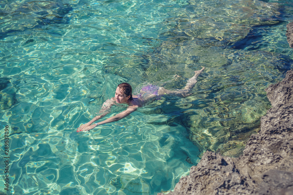 Young European woman in a colorful bikini swimming in clear blue water in sea. She is enjoying her summer holidays.