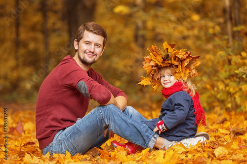 Father and daughter. They sit in the park and play with the leaves. Spending time together.