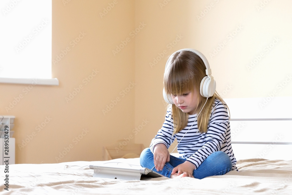 Naklejka premium Little sitting girl using tablet with headphones