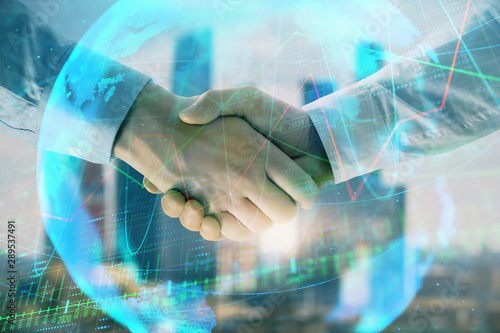 Double exposure of financial chart and world map on cityscape background with two businessmen handshake. Concept of international investment © Andrey