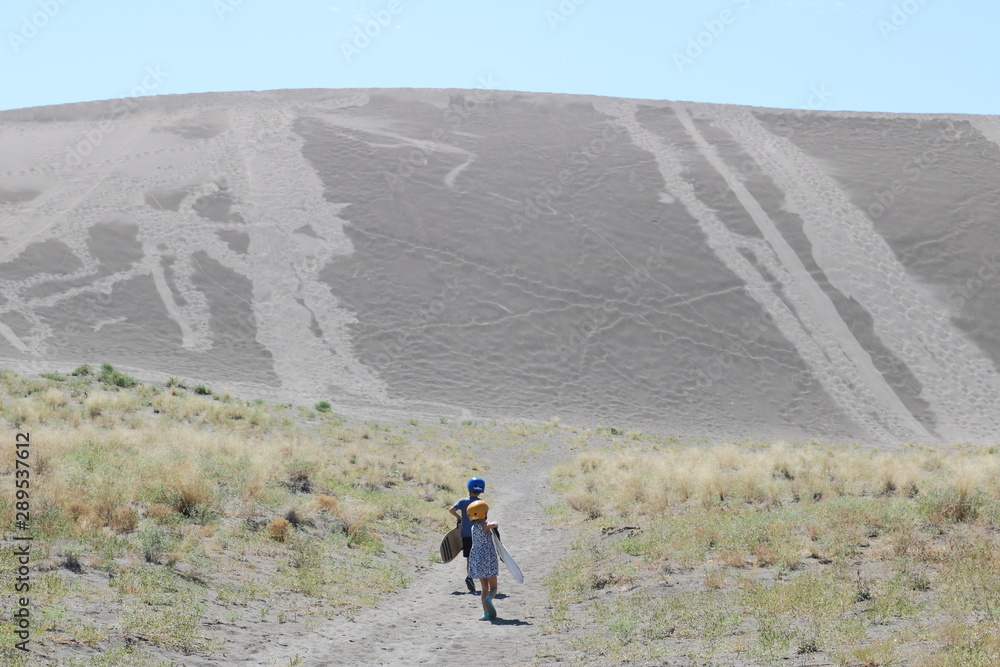 Two kids wearing helmets and carrying their boards to go sandboarding in Bruneau, Idaho Two kids wearing helmets and carrying their boards to go sandboarding in Bruneau, Idaho
