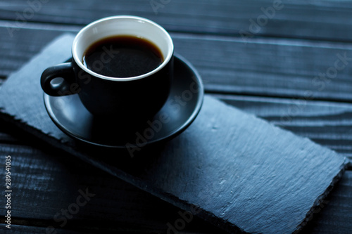 Espresso coffee in a small black cup on a stone stand on a black wooden table, selective focus