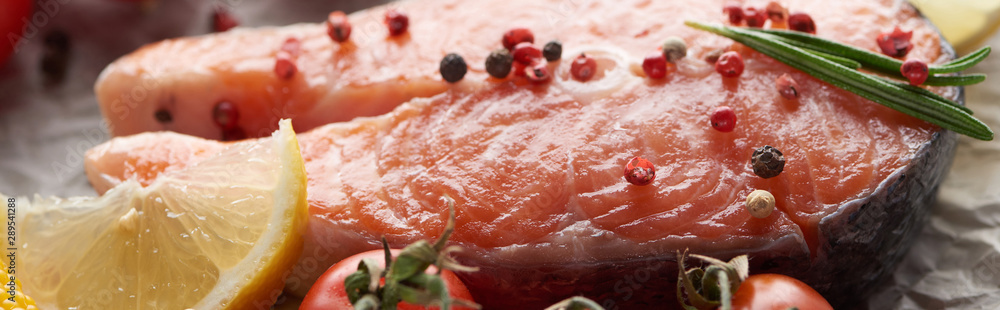 close up view of raw salmon steak with peppercorns, lemon and rosemary, panoramic shot close up view of raw salmon steak with peppercorns, lemon and rosemary, panoramic shot