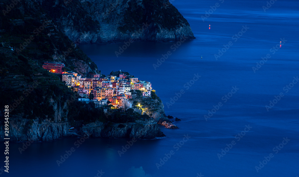 The fishing village of Manarola in Cinque Terre, Italy, illuminated at dusk during blue hour with the Mediterranean sea as background