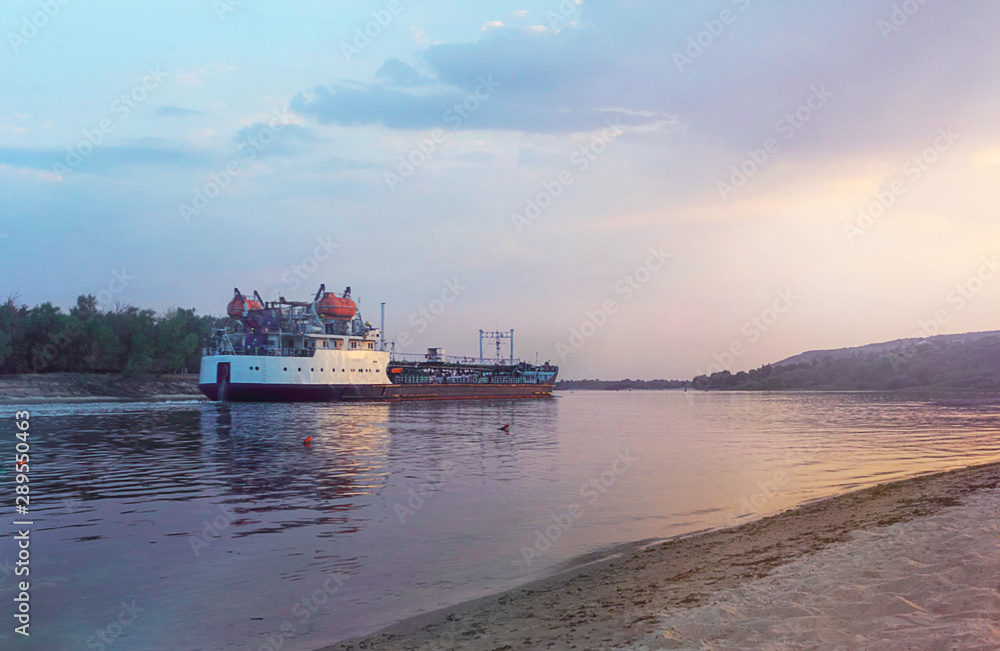 Barge with cargo on the river. Colorful sky with clouds, skyline, sunset, panorama.