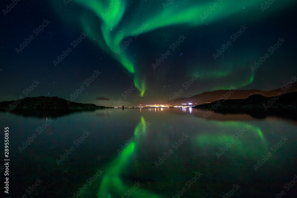 Green Northern lights reflecting in the lake with mountains and city in the background, Nuuk, Greenland