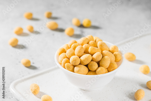 Peanuts in cheese sauce in a white bowl on a light gray table