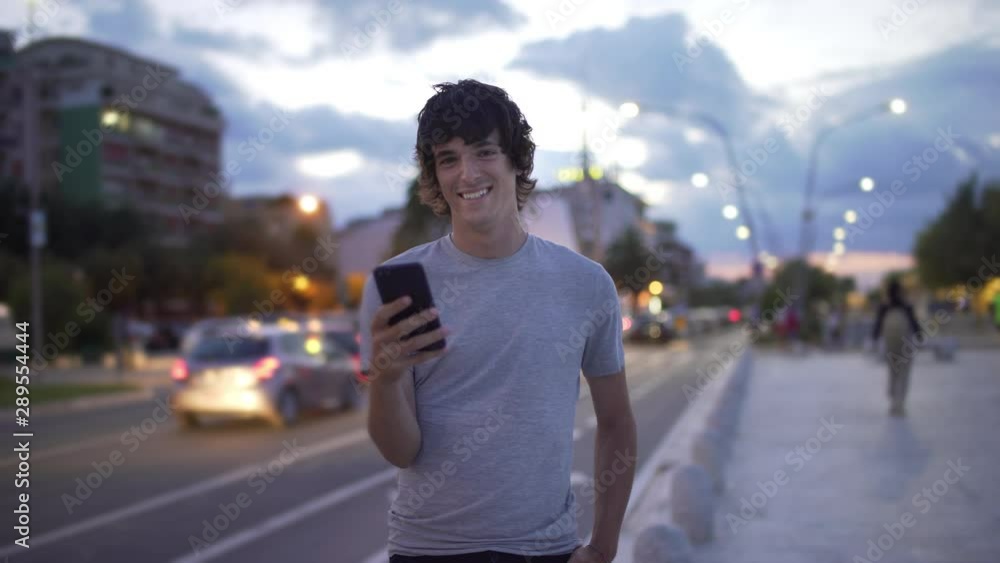 Handsome urban guy using cellphone or smartphone and smiling in the city at night. Attractive young man using smart phone and smiling happly wearing a blue shirt and a t shirt. Handsome urban guy using cellphone or smartphone and smiling in the city at night. Attractive young man using smart phone and smiling happly wearing a blue shirt and a t shirt.
