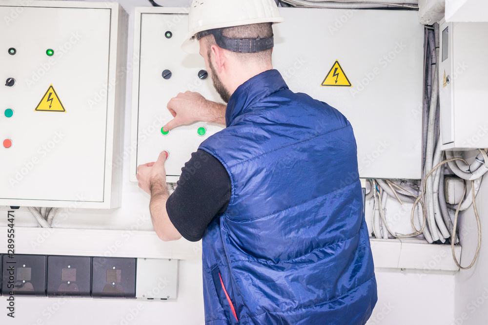 Technician checks the electrical supply system. The engineer presses the buttons of the electric control panel. Electrician works near fuse box. View from the back. Technician checks the electrical supply system. The engineer presses the buttons of the electric control panel. Electrician works near fuse box. View from the back.