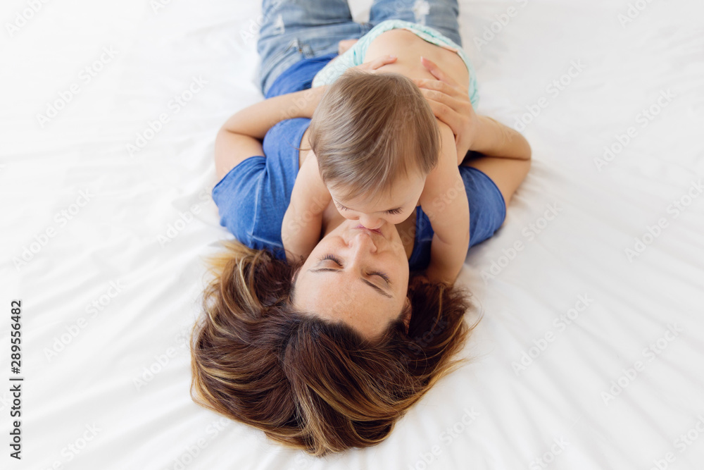 Overhead view of mother lying on bed holding and kissing her baby Overhead view of mother lying on bed holding and kissing her baby