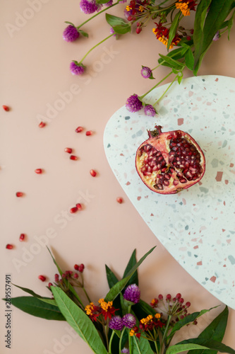 styled still life flat lay photo with cut pomegranate, fresh flowers, terrazzo dish, and pink background