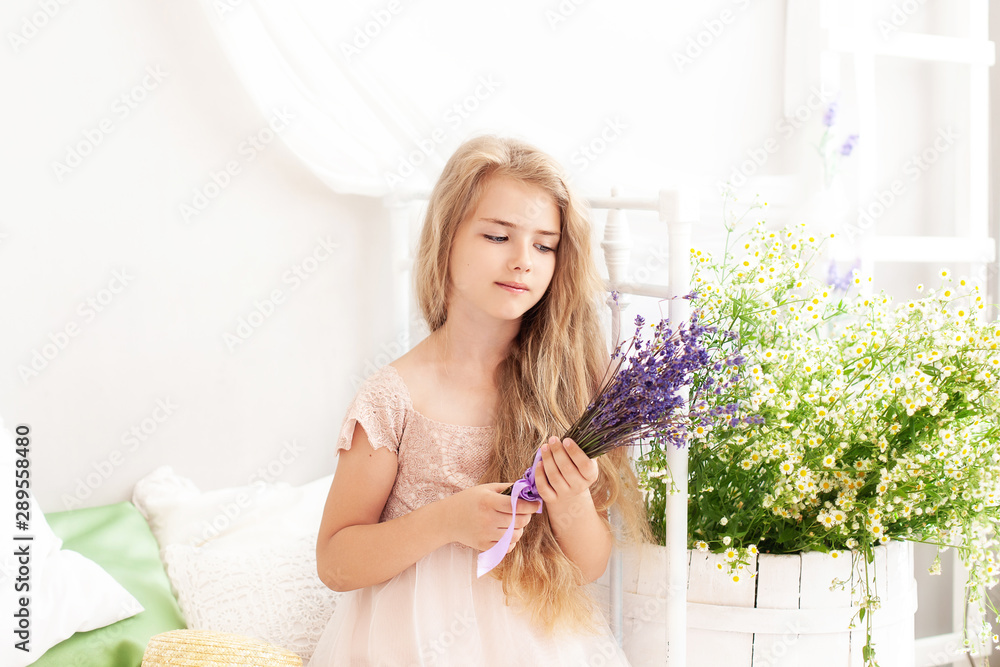 Rustic style bedroom, provence style. Childhood concept. Cute little girl in a dress holds a bouquet of lavender in her hands. A child sits on a bed in his nursery against a background of daisies. Rustic style bedroom, provence style. Childhood concept. Cute little girl in a dress holds a bouquet of lavender in her hands. A child sits on a bed in his nursery against a background of daisies.