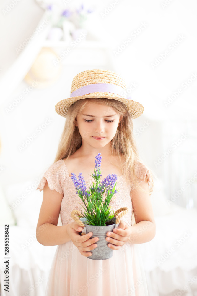 Cute little girl with long blond hair in a straw hat in a dress holds pot of lavender. Childhood concept. Gardening. floriculture. Environmental Protection. Hobby. Summer flowers, houseplant lavender