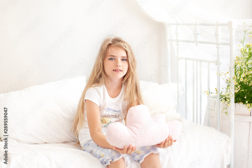 Childhood concept. Child playing in bed in a white bedroom. Children's room and interior design. Little girl in pajamas at home. Toddler with a toy. sleep time. blond girl in cozy scandinavian bedroom