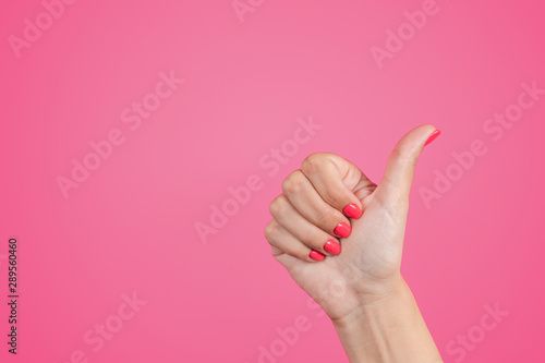 Closeup view of beautiful female hand isolated on pink background. Woman making like gesture raising thumb up cheerfully as sign of like and success. Horizonal color photography.