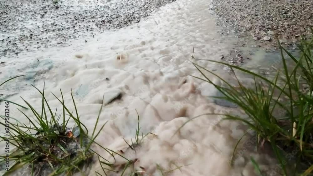 Muddy rain water flowing off a concrete drive to the edge of a road and onto grass, rippling over pebbles with rain drops splashing around Muddy rain water flowing off a concrete drive to the edge of a road and onto grass, rippling over pebbles with rain drops splashing around