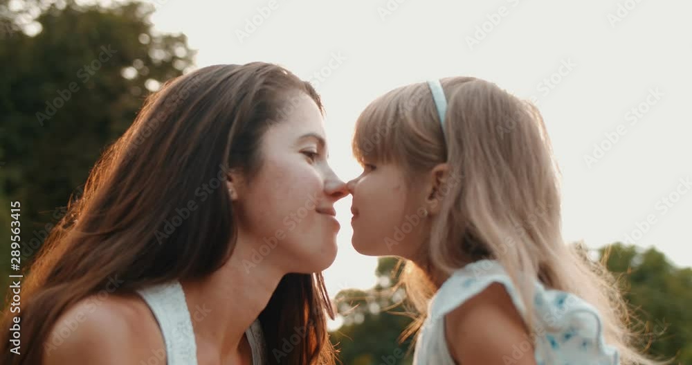 Portrait of the beautiful Caucasian young mother kissing and hugging her small cute daughter and they smiling to the camera in the park. Close up. Portrait of the beautiful Caucasian young mother kissing and hugging her small cute daughter and they smiling to the camera in the park. Close up.